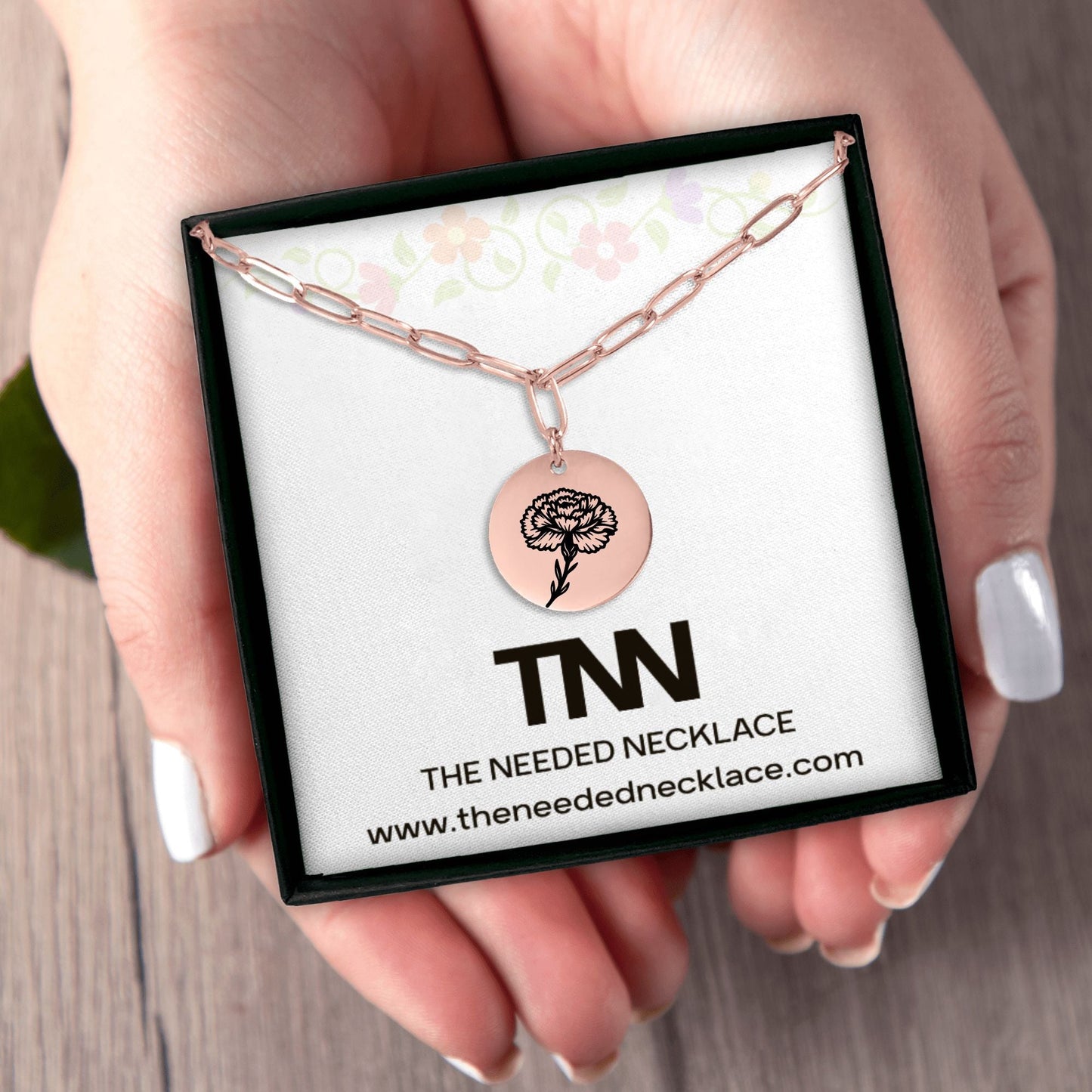 Rose gold necklace with circular pendant on a branded card held by a hand.
