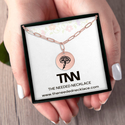 Rose gold necklace with circular pendant on a branded card held by a hand.